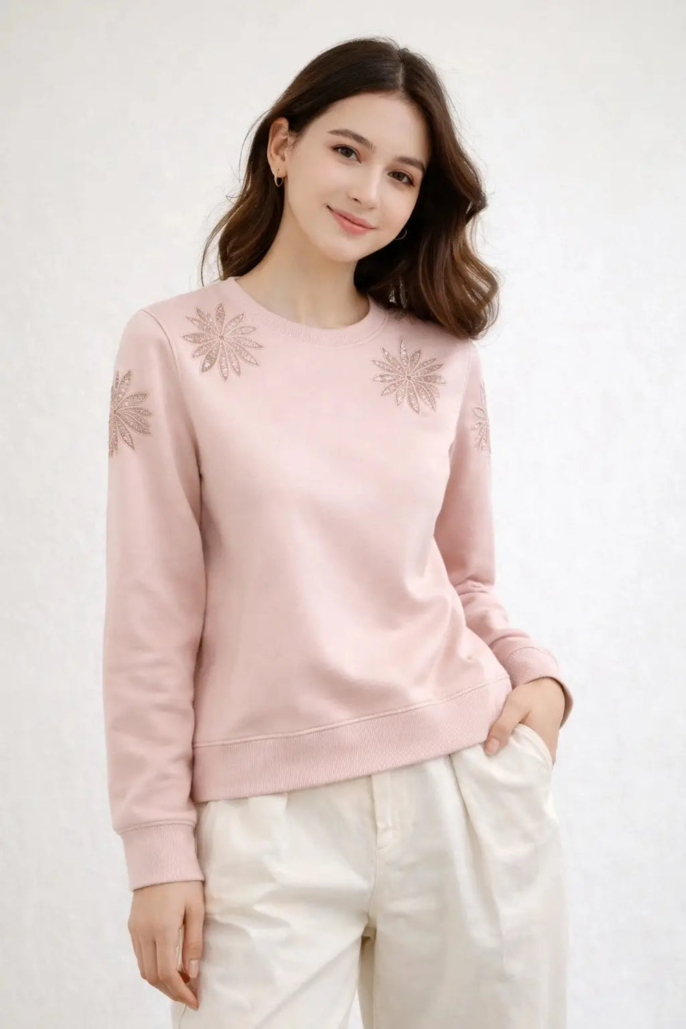 Woman wearing a pink sweater with floral embellishments on a white background