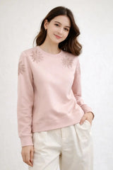 Woman wearing a pink sweater with floral embellishments on a white background
