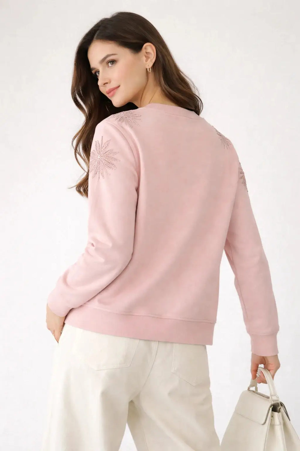 Woman wearing a pink sweatshirt and white pants on a white background