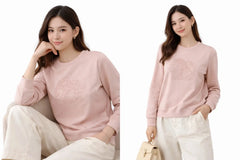 Two images of a woman wearing a pink sweater with floral patterns, sitting and standing.