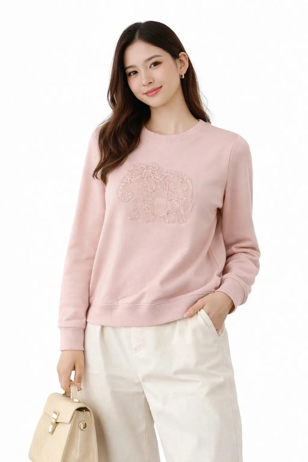 Woman wearing a pink sweater with a logo, holding a beige handbag on a white background