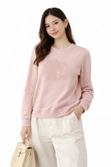 Woman wearing a pink sweater with a logo, holding a beige handbag on a white background