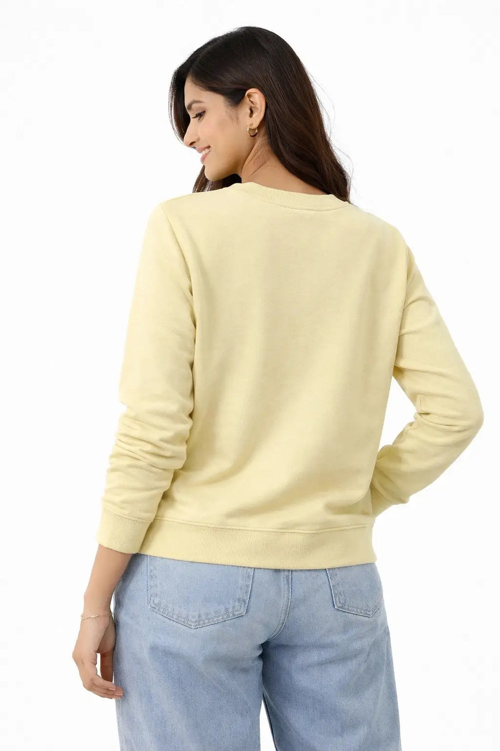 Woman wearing a light yellow sweatshirt and light blue jeans on a white background