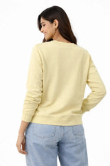 Woman wearing a light yellow sweatshirt and light blue jeans on a white background