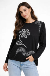 Woman wearing a black long-sleeve top with floral design and light blue jeans on a white background