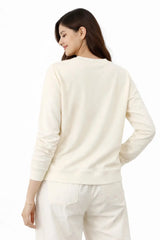 Woman wearing a cream-colored sweater and pants on a white background