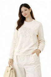 Woman wearing a white sweater and pants with a beige handbag on a white background