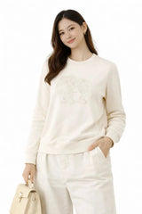 Woman wearing a white sweater and pants with a beige handbag on a white background