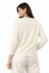 Woman wearing a cream-colored sweater and pants on a white background