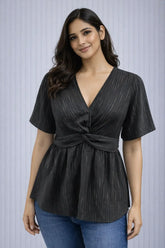 Woman wearing a black top with a tie detail and blue jeans on a light gray background