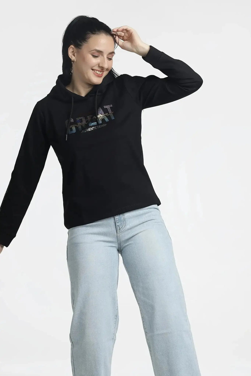 Woman wearing a black hoodie with text and light blue jeans on a white background