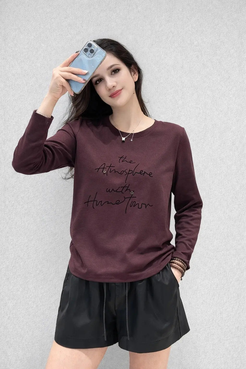 Woman wearing a maroon long-sleeve shirt with text and black shorts against a light gray background