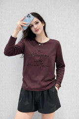 Woman wearing a maroon long-sleeve shirt with text and black shorts against a light gray background