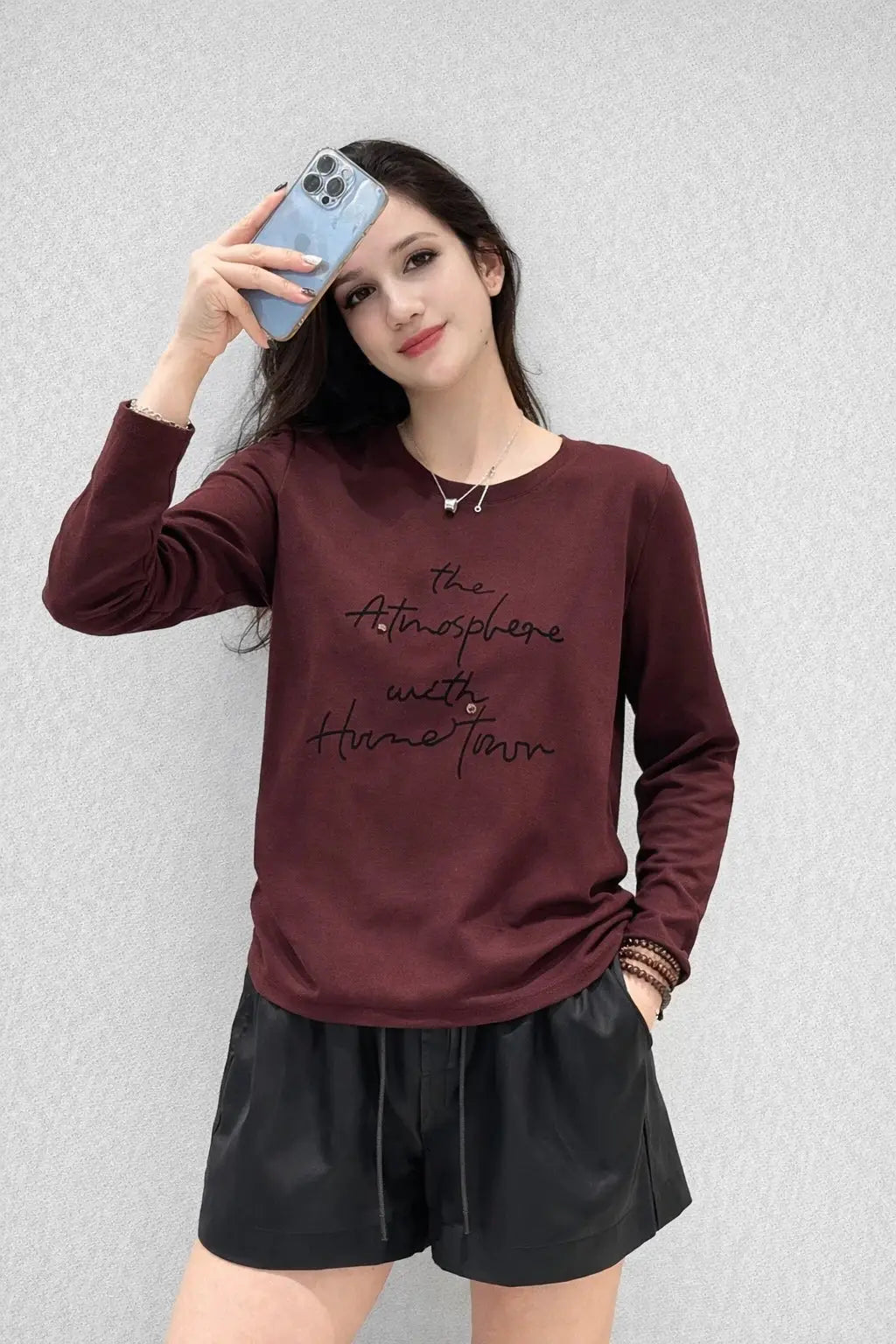Woman wearing a burgundy sweatshirt with text and black shorts against a light gray background