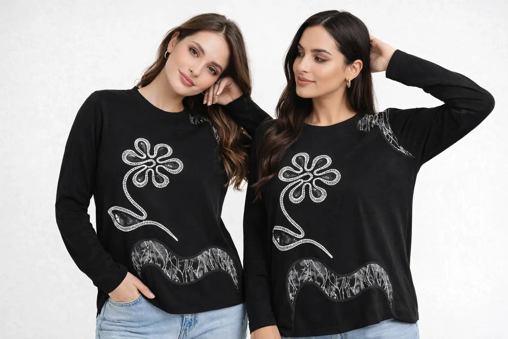 Two women wearing black sweatshirts with white floral designs on a plain background