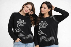 Two women wearing black sweatshirts with white floral designs on a plain background