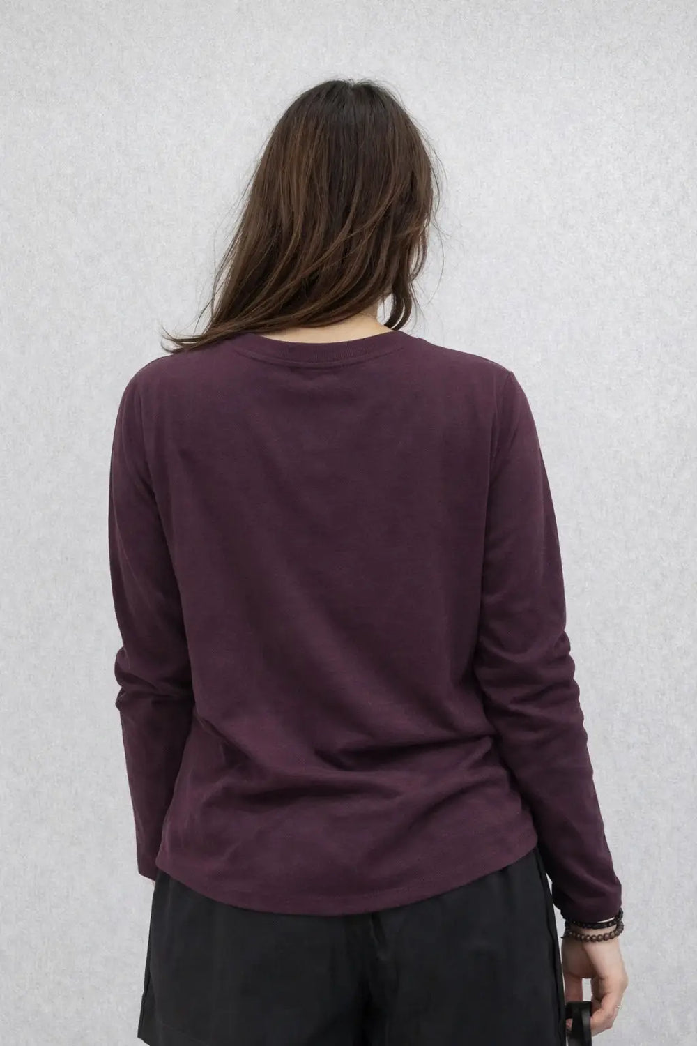 Person wearing a purple long-sleeve shirt against a light gray background