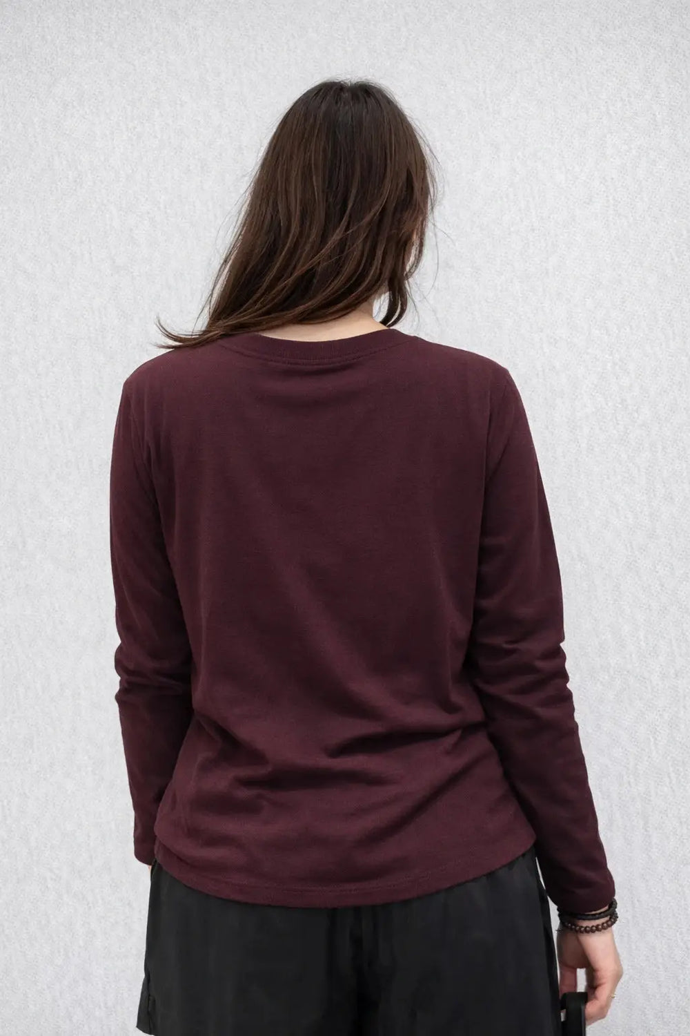 Person wearing a maroon long-sleeve shirt against a light gray textured wall.